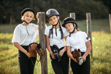 Portrait of girls jockeys sitting on toy horses near a wooden post