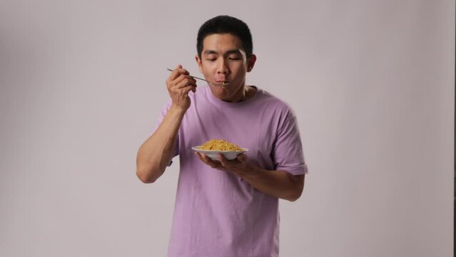 A man from Indonesia, Asia, wearing a purple t-shirt, appears to be enjoying noodles by slurping them. Isolated on a white background.
