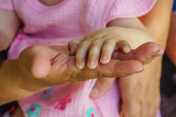 Close-up of a small child's hand on the palm of an old grandmother. A gesture signifying support...