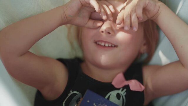 A fair-skinned blue-eyed girl enjoys a sunny morning in the hammock. A close-up slow-motion shot.