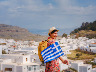 Young traveling woman with national greek flag enjoying view of Lindos. Travel to Greece,...