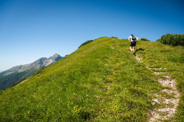 A young adventurer confidently strides along the lush green ridge of the Belianske Tatras, gazing out towards the majestic High Tatras on the horizon