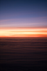 Fototapeta na wymiar A radiant sunset, as seen from an airplane high above the clouds. The sky is a gradient of bluish purple and reddish orange. The light reflects off the tops of the clouds.