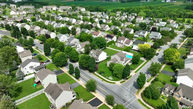 Wide shot of large American neighborhood full of family houses and homes. Mature trees and grass in summer. Beautiful aerial establishing shot of community housing development in USA.