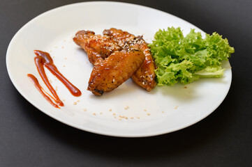 Caramelized chicken wings on a plate with salad and barbecue sauce