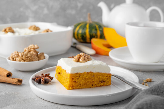 Spiced pumpkin cake with walnut and cream cheese frosting sliced into squares on a gray concrete background. Autumn dessert.