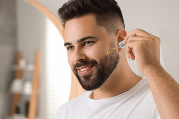 Handsome man applying cosmetic serum onto his face in bathroom