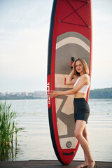 Woman is standing with sup board against the lake