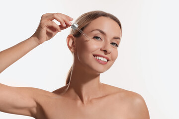 Beautiful woman applying cosmetic serum onto her face on white background