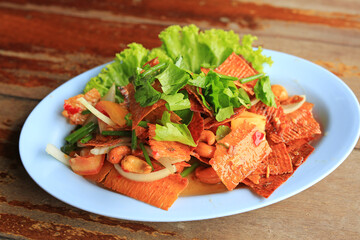 Dried spicy squid cuttlefish salad with cashew nuts and fresh vegetables in plate on wood table. Thai style food.