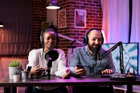 African american woman and cohost during online show in neon lights studio, shooting vlog using professional recording tools. Vloggers talking with fans during live broadcast - Powered by Adobe
