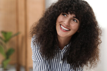 Portrait of beautiful woman with curly hair indoors. Attractive lady smiling and posing for camera. Space for text