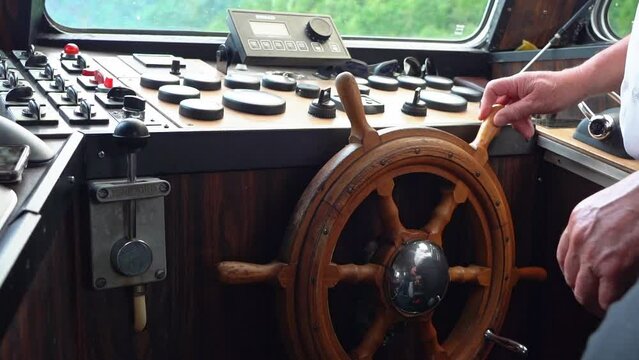 Hands turning old fashioned wooden helmsman wheel on a boat - Handheld closeup of Wheel inside wheelhouse