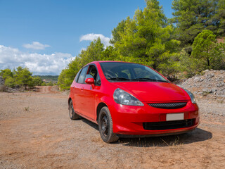 A red subcompact car stands in the mountains in Greece