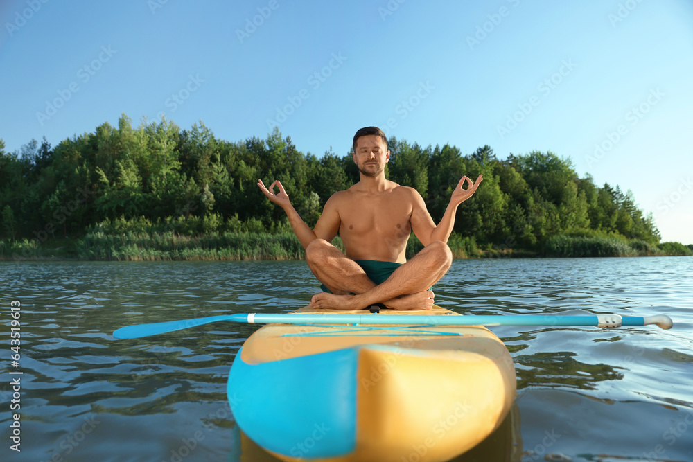 Wall mural Man meditating on color SUP board on river