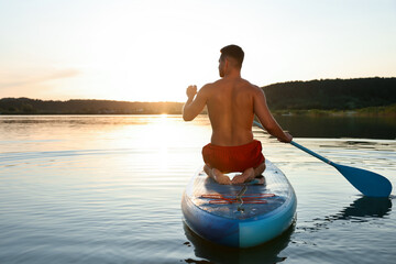 Man paddle boarding on SUP board in river at sunset, back view