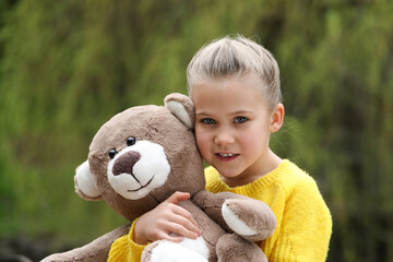 Cute little girl with teddy bear outdoors