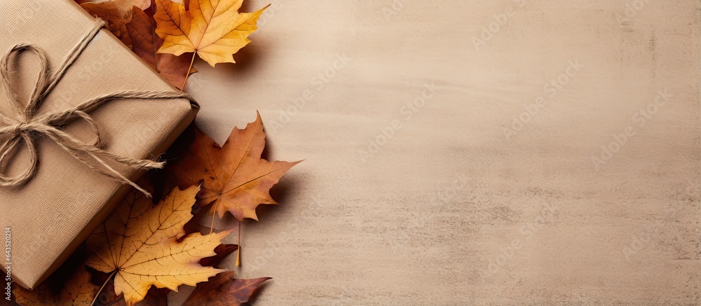 Poster autumn arrangement featuring dried leaves a wrapped gift placed in a corner on rustic linen backgrou