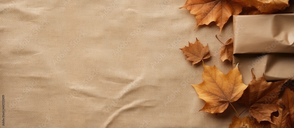 Poster autumn arrangement featuring dried leaves a wrapped gift placed in a corner on rustic linen backgrou