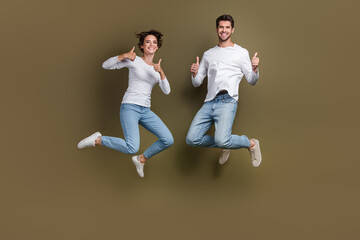 Full length photo of positive confident wife husband dressed white shirts jumping thumbs up empty space isolated brown color background