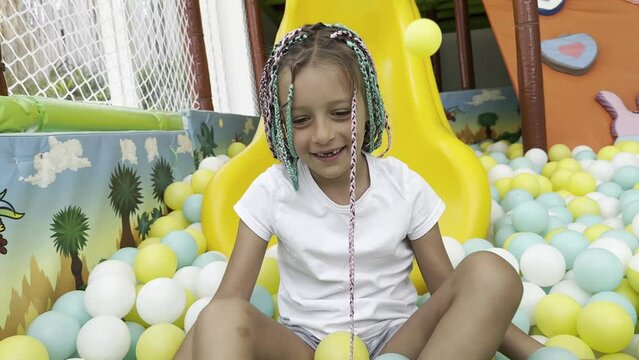 Happy laughing girl kid having fun at indoor play center. Child playing with colorful  balls in playground ball pool. child in white t-shirt.