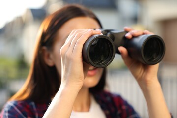Concept of private life. Curious young woman with binoculars spying on neighbours outdoors, closeup