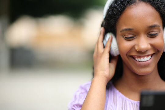 Happy black woman listening audio on phone in the street
