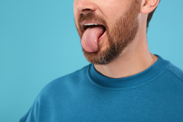 Obraz premium Man showing his tongue on light blue background, closeup