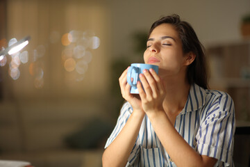 Woman smelling hot coffee at home in the night
