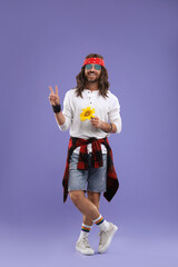 Stylish hippie man with sunflower showing V-sign on violet background