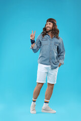Stylish hippie man showing V-sign on light blue background