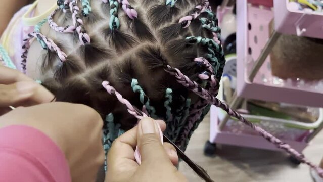 Hands masters make for small girl many african braids. Woman in hair salon plaits pigtails. Hairstyle fashion style for children. Decorating beads. Close up.
