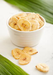 Yellow dried banana chips snack in glass bowl plate on light background