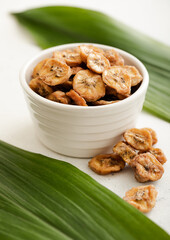 Dried fresh organic banana slices in glass bowl with green leaf.Macro
