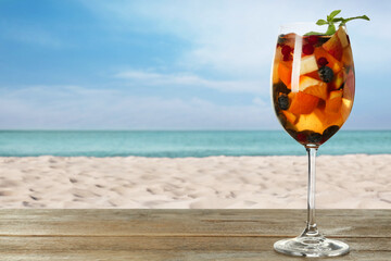 Refreshing Red Sangria on wooden table near sea, space for text