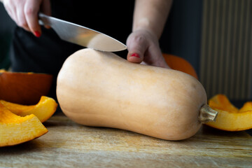 Woman cutting butternut squash pumpkin into slices with a kitchen knife on a wooden board. Fresh...