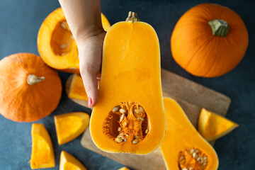 Woman holding sliced butternut squash. Cutting pumpkin into slices. Fresh raw pumpkins pieces cut in half. Preparing food ingredients for a seasonal autumn fall dish, soup or pie. - obrazy, fototapety, plakaty
