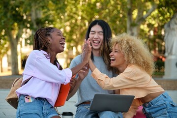 Three happy multiracial friends high five and laughing because got a perfect test score at a park.