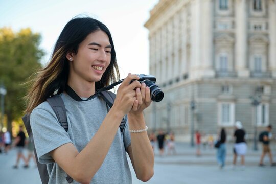 Asian male tourist smiling and looking at photos in his camera while sightseeing in Madrid, Spain.