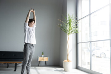 Full body of man stretching and elongating by the window in the morning sun