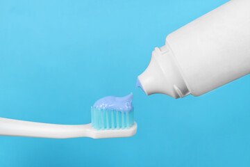 Fototapeta na wymiar Applying paste on toothbrush against light blue background, closeup
