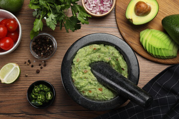 Delicious guacamole in mortar and ingredients on wooden table, flat lay