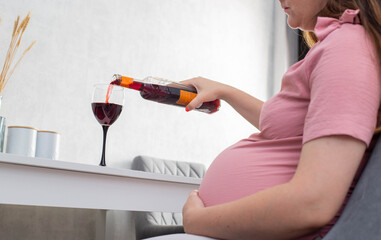 A pregnant girl pours wine from a bottle into a glass. The concept of drinking alcohol during...