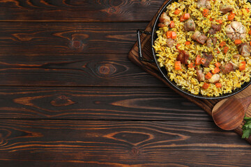 Delicious pilaf with meat, carrot and garlic served on wooden table, top view. Space for text