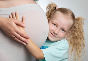 The daughter hugs the big belly of the pregnant mother in anticipation of the birth of her brother, close-up