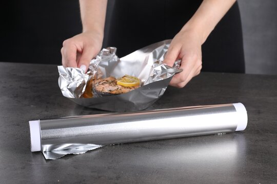 Aluminum foil and woman with tasty salmon at grey textured table, closeup