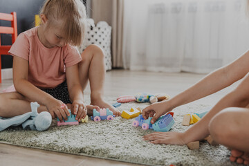 Children playing with colorful plastic toy colourful train. Kids sitting on carpet indoors at sunny white home bedroom or kindergarten, nursery. Funny educational eco-friendly game for child
