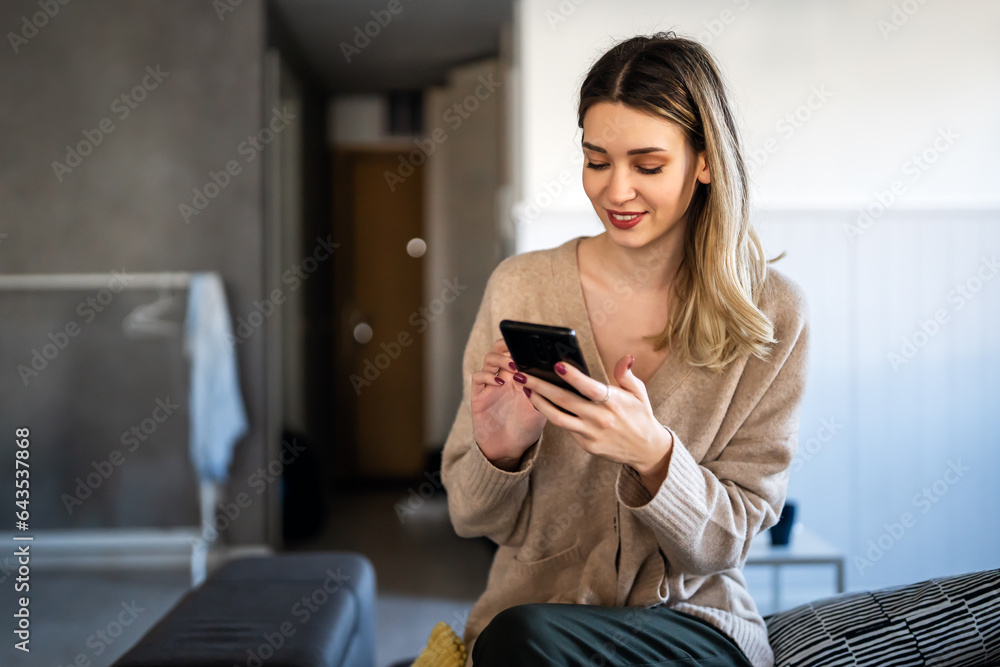 Wall mural Smiling young woman chatting in social networks, working, using mobile applications at home.