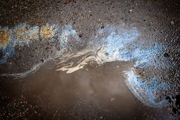 Leakage of oil or gasoline from under the car on the asphalt in the parking lot.
