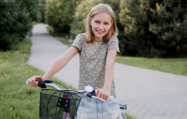 Cute preteen girl with bycicle outdoors looking at camera and smiling. Pretty child with bike at city street at summer park